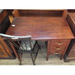 A stained oak three drawer desk with a folding leaf and an upholstered stick back chair