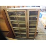 A large light oak glazed two door cupboard with adjustable shelves