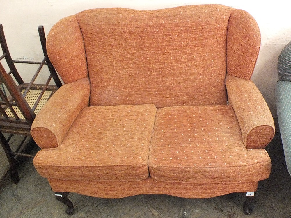 A two seater wingback sofa with terracotta upholstery and cabriole legs