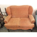 A two seater wingback sofa with terracotta upholstery and cabriole legs