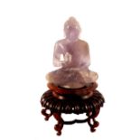 A carved mauve quartz seated Buddha on wooden stand