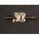 An unmarked gold bar brooch with large monogram centre encrusted with diamonds