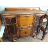 A 1930's oak carved and glazed bookcase with unusual drop leaf writing desk feature to the centre