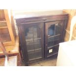 A dark stained oak bookcase with two glazed doors on bun feet (as found)