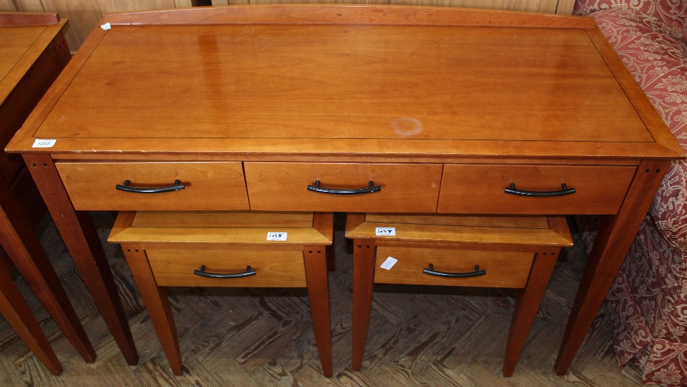 A modern three drawer writing desk and a pair of bedside tables with single drawers