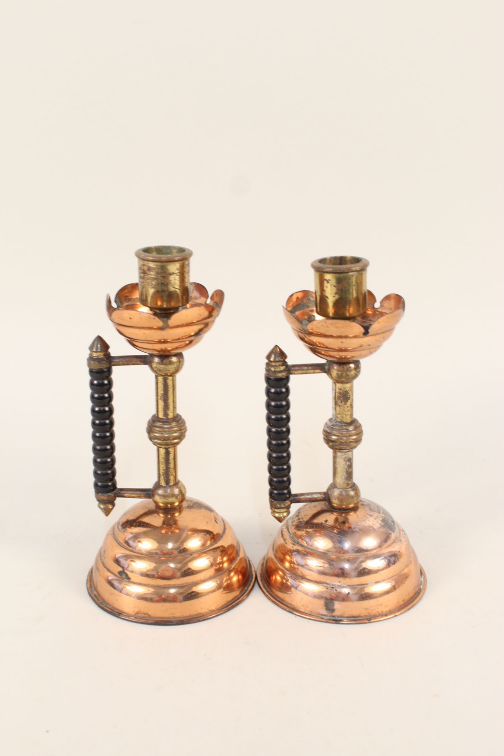 A pair of Arts and Crafts copper and brass candlesticks with bobbin turned ebonised side handles,