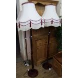 A pair of maroon painted wooden standard lamps with large white and maroon tasselled lampshades