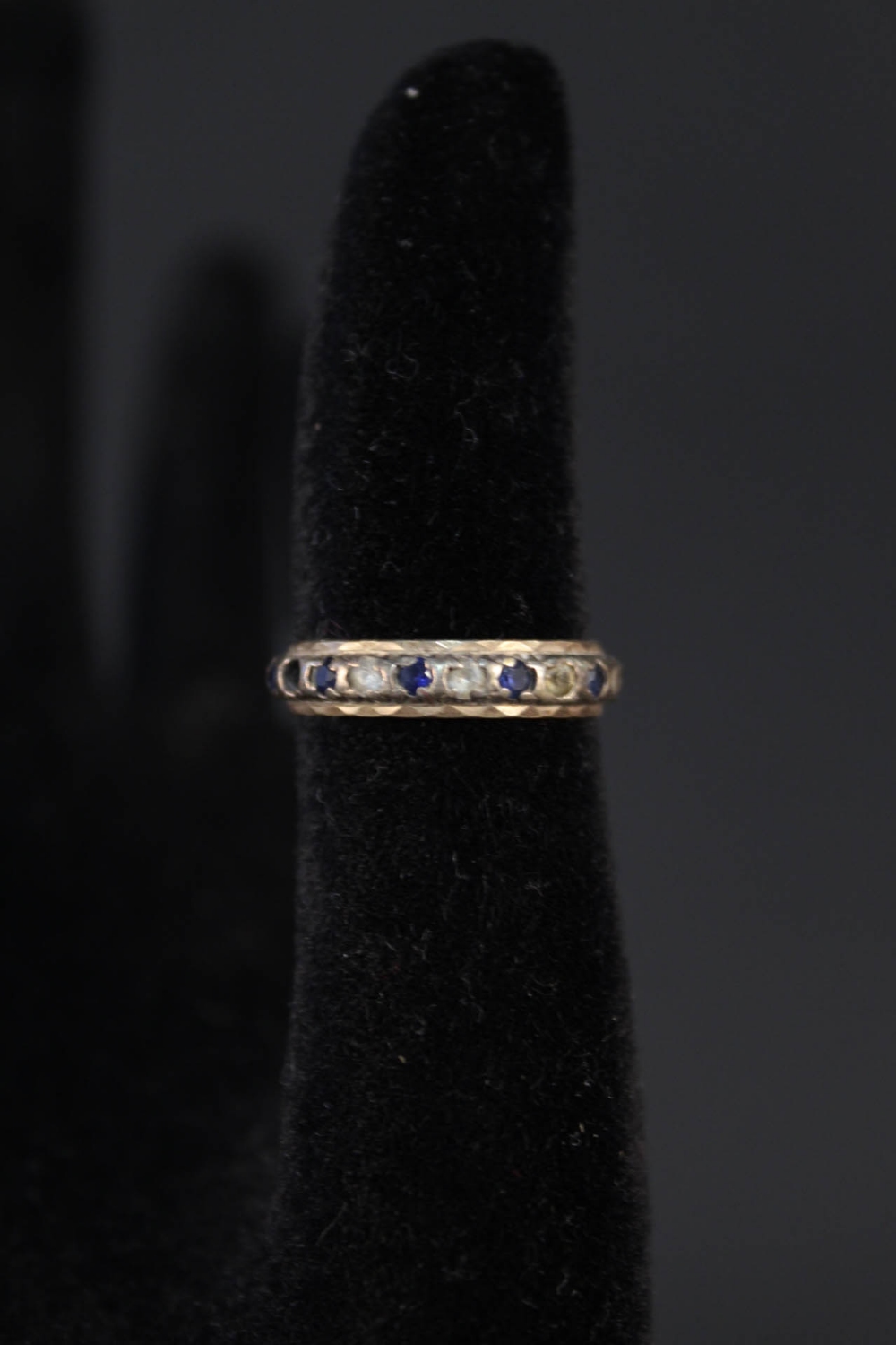 A yellow and white metal eternity ring set with blue and white stones,