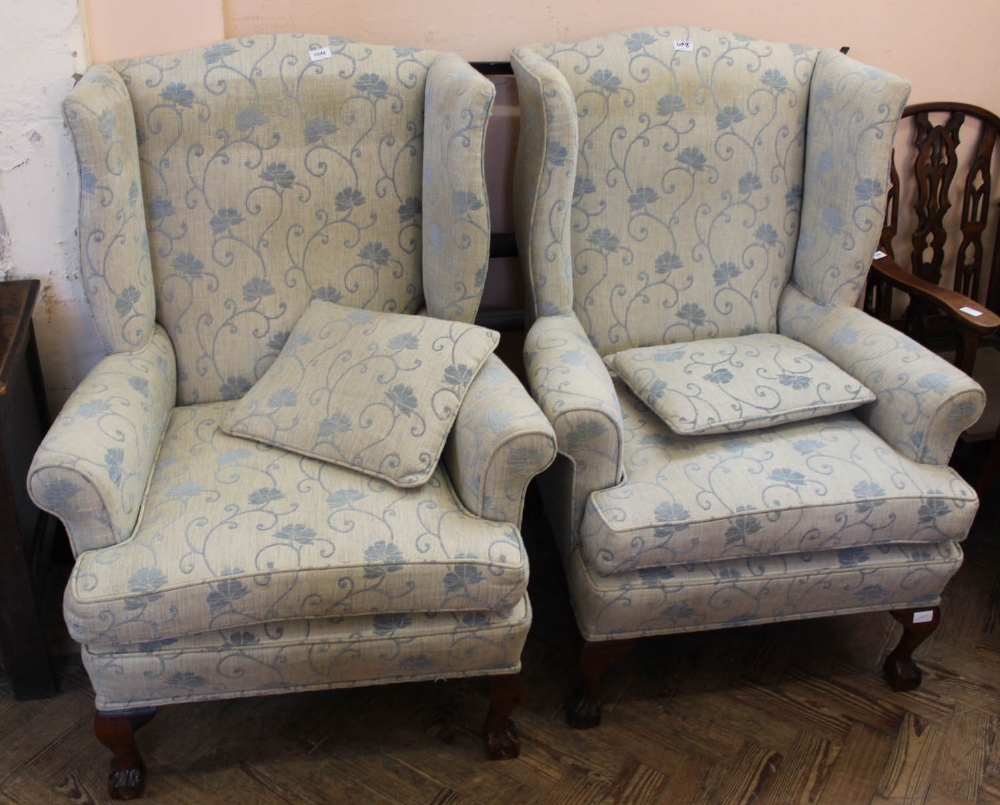 A pair of pale blue floral upholstered wingback chairs with oak claw and ball feet