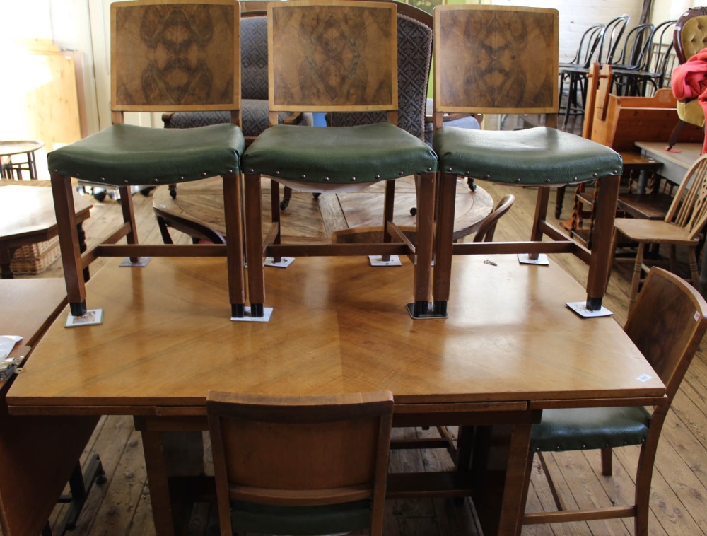 An Art Deco figured walnut draw leaf dining table on solid end supports and a set of six matching