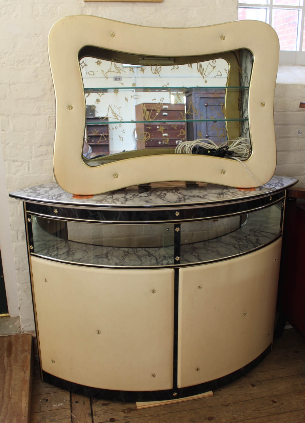 A 1950's white vinyl and glass mini bar with matching mirror and glass wall mounted shelving unit