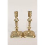 A pair of early 18th Century seamed brass candlesticks with knopped stems and canted square bases,