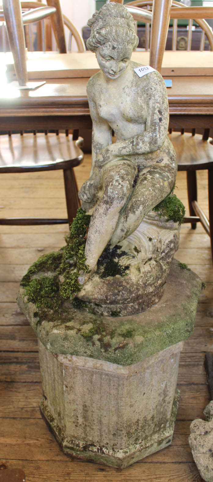 A weathered garden statue of a seated lady