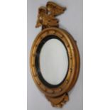 A 19thC gilt wood porthole mirror, surmounted by heavily carved eagle, the round bevel glass with an