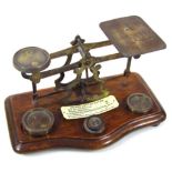 An early 20thC brass postal scale, on serpentine shaped oak stand, with a variety of weights, 21cm
