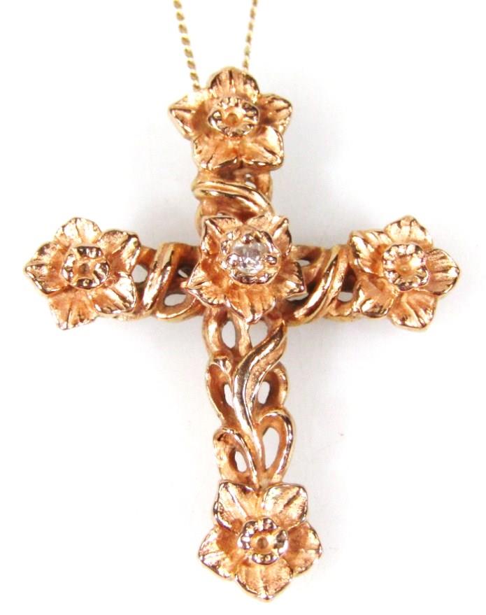 A gold crucifix pendant, on a fine link chain, the crucifx with floral design, set with tiny diamond