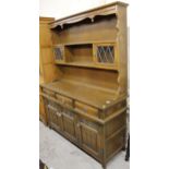 An Ercol style linen fold dresser, the upper section with a carved cornice above two Delft racks,