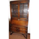 A 1920's oak bureau bookcase, the upper section with a moulded caddy top above glazed cupboard