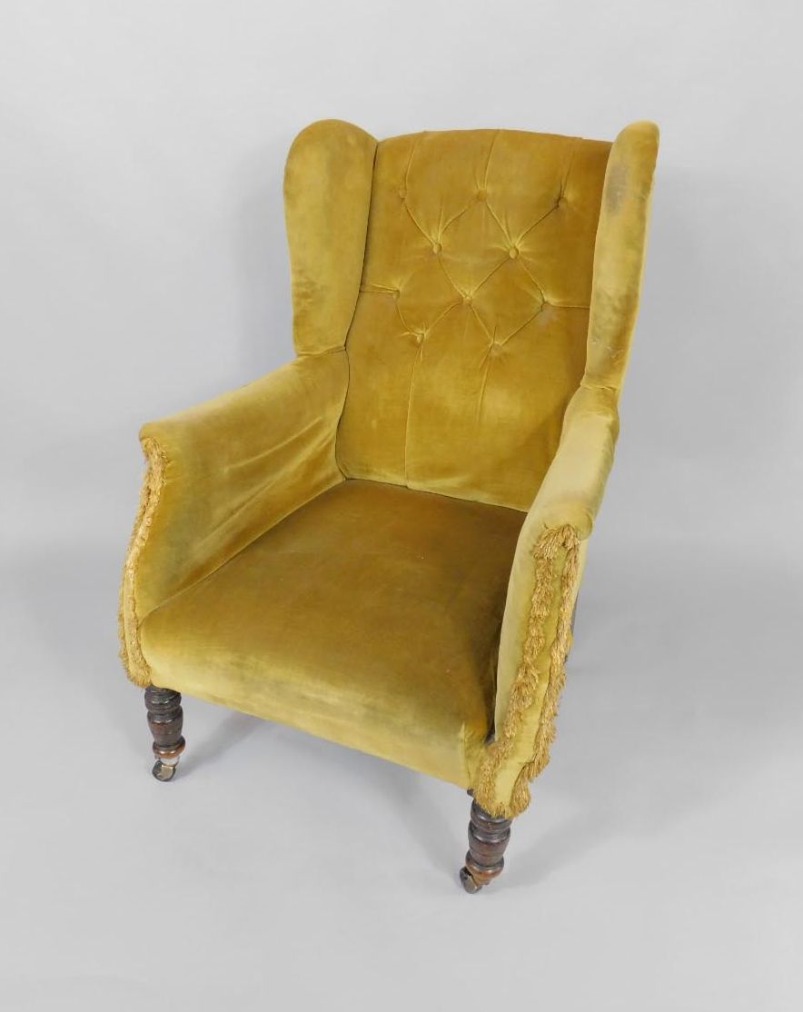 A Victorian mahogany framed wingback library armchair, upholstered in yellow fabric, raised on