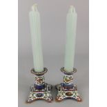 A pair of champleve dwarf candlesticks, decorated with birds, leaves, flowers etc on a square