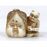A Japanese carved ivory netsuke, of a seated oni holding a large face mask and a bowl in his lap,