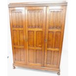 An early 20thC oak triple wardrobe, with carved linen fold panels, doors, on bun feet, 150cm wide