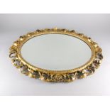 A Florentine giltwood wall mirror, with an oval bevelled plate, decorated with scrolls, shells etc.,