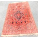 A Persian style rug, with a design of flowers around a central pearl medallion on a red ground,