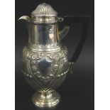 A late Victorian silver hot water pot, embossed with flowers, fluting etc., with an ebonised