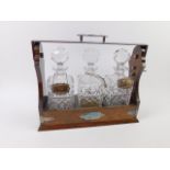 An oak three bottle Tantalus, with plated mounts, square cut glass decanters and stoppers, with