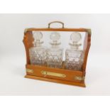 An oak and brass mounted three bottle tantalus, containing three square cut glass decanters and