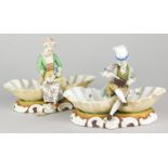 A pair of 19thC German porcelain salts, in the form of a gentleman and lady preparing food beside