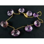 An amethyst necklace, with eight rough cut amethyst stones, on a fine link yellow metal chain,