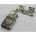 A silver locket, the locket with gold coloured crest design, on a silver plated chain.