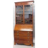 An early 19thC mahogany bureau bookcase, the overhanging inlaid fixed cornice raised above a pair of