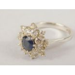 An 18ct white gold (stamp) sapphire and diamond cluster ring, a central dark sapphire of 5.6mm x 4.