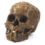 A hand carved tribal skull, with shaped scroll head, 18cm H.