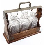 An Edwardian oak and chrome plated tantalus, holding three decanters, each cut glass with orb