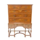 A William & Mary style walnut and mahogany cross banded chest on stand, the pediment over two