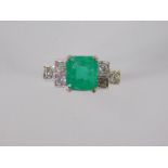 An emerald and diamond ring, the square cut emerald flanked by three stepped diamonds to the