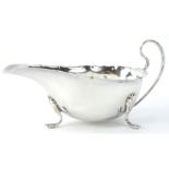 A George V silver sauce boat, with a shaped border, scroll handle and three feet, Birmingham 1930,