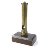 A locomotive railway whistle, with cylindrical outline in brass on wooden stand, 25cm H.