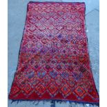 A Moroccan carpet, with a multi-coloured designs of lozenges on a red ground, 265cm x 150cm.