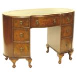 An early 20thC walnut kidney shaped desk, the top with a green leather inset above an arrangement of