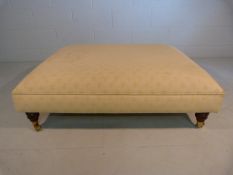 Large low upholstered footstool on brass castors