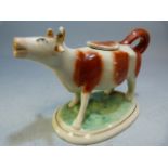 Early 19th century Staffordshire creamware cow creamer. Red painted cow with gilded horns on a green