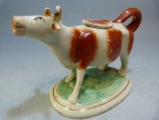 Early 19th century Staffordshire creamware cow creamer. Red painted cow with gilded horns on a green