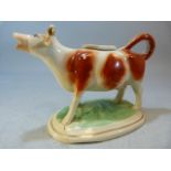 Early 19th century Staffordshire creamware cow creamer. Red painted cow with gilded horns on a green