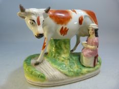 19th Century Staffordshire figure group of a large cow and milk maid sat beneath. Red and cream