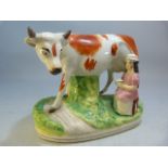 19th Century Staffordshire figure group of a large cow and milk maid sat beneath. Red and cream